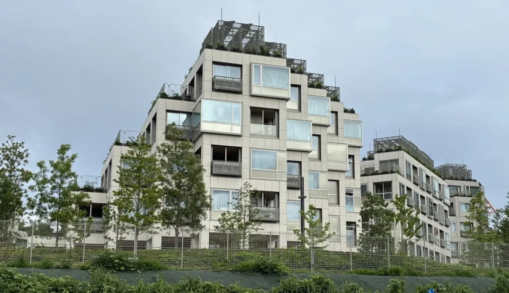 白い外壁に凹凸のある窓が並ぶウーブン・シティの住居棟。屋上には植栽とルーバーが施されている