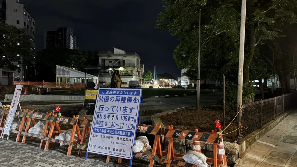 沼津市中央公園の再整備工事の案内看板と、夜の現場に停まる小型ショベルカー