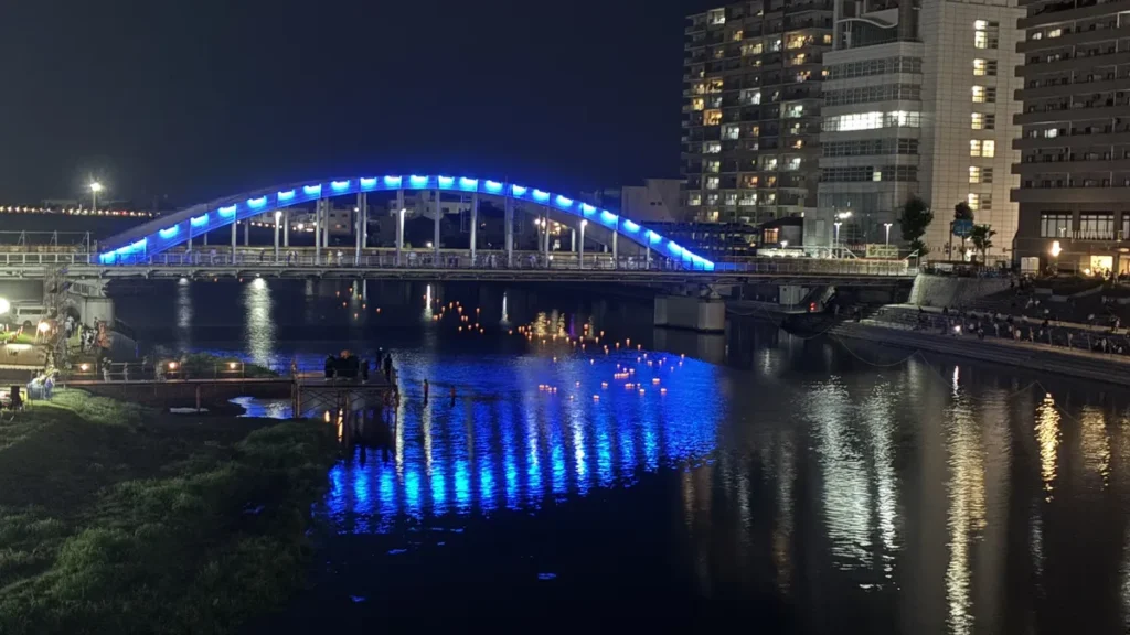青くライトアップされた御成橋と、その下を流れる灯ろう(沼津・狩野川の灯ろう流し)