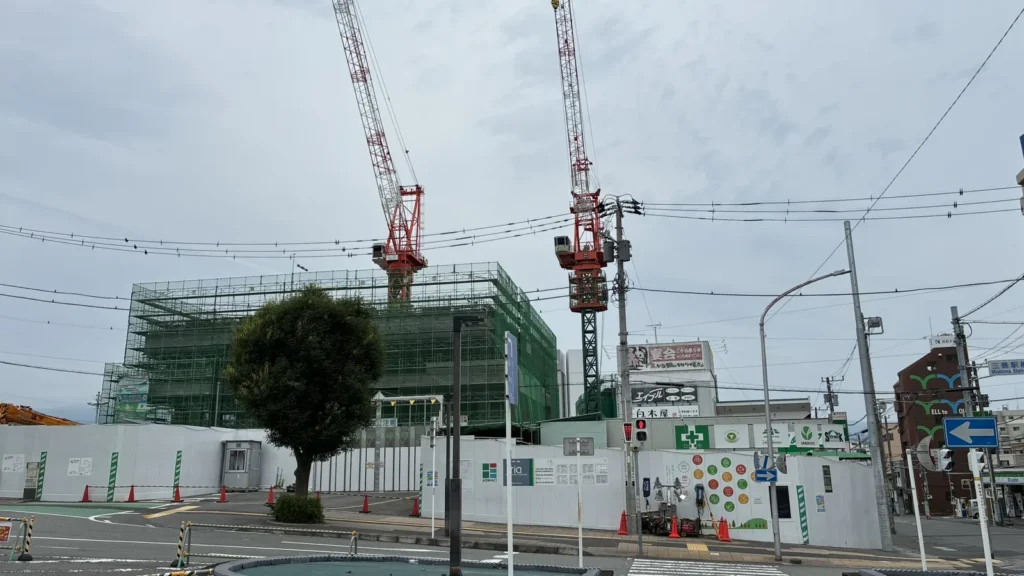 三島駅南口東街区A地区の建設現場。タワークレーン2基と緑の養生ネットに覆われた躯体