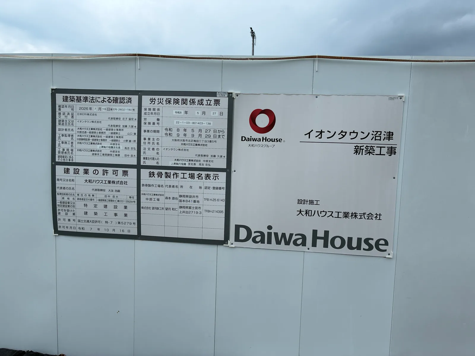 仮囲いに貼られた「イオンタウン沼津 新築工事」の看板と、建築基準法による確認済、労災保険関係成立票、建設業の許可票、鉄骨製作工場名表示