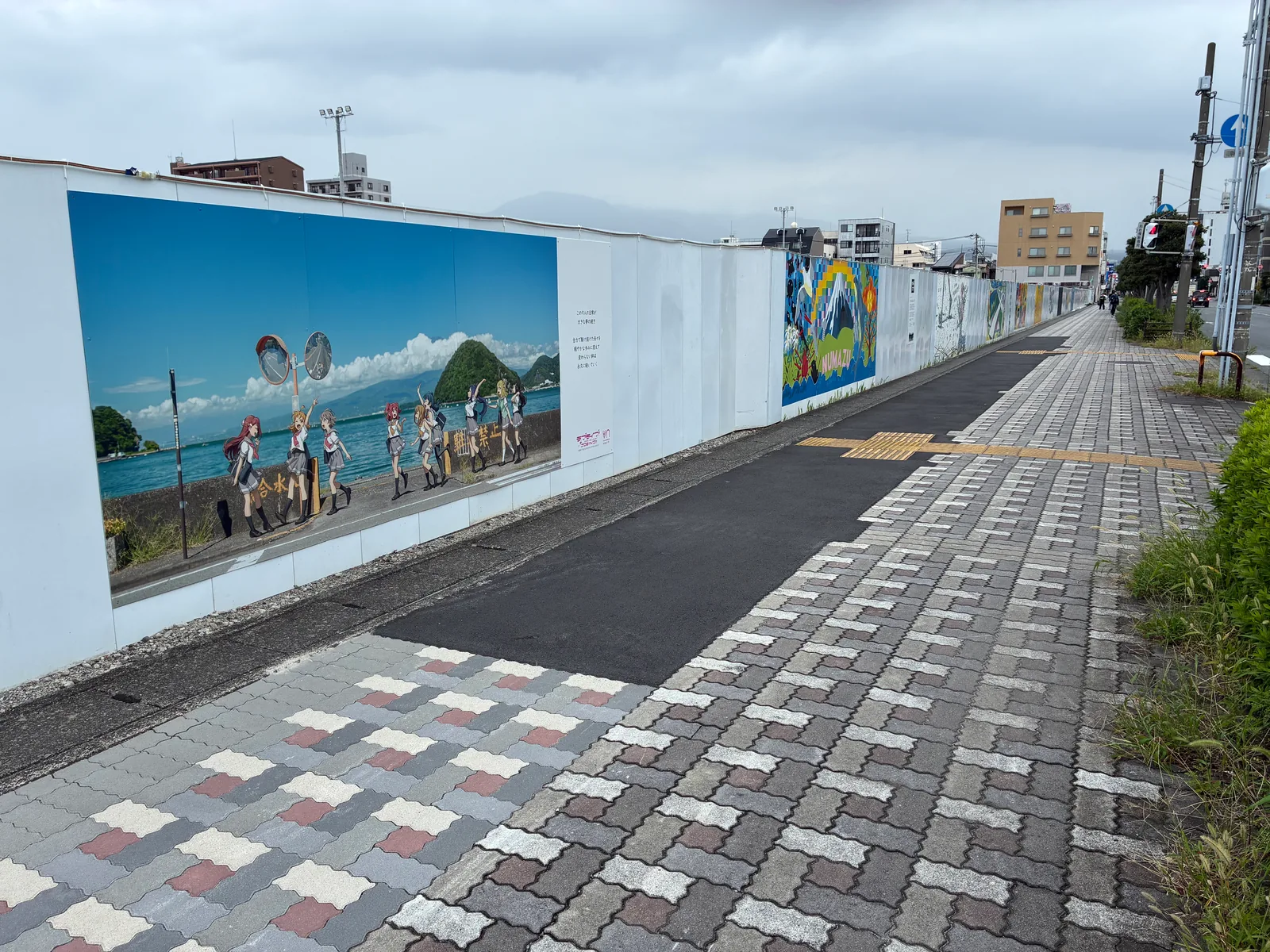 壁画が続く工事の仮囲いと、その横の広いインターロッキングの歩道。南側から北を見た様子