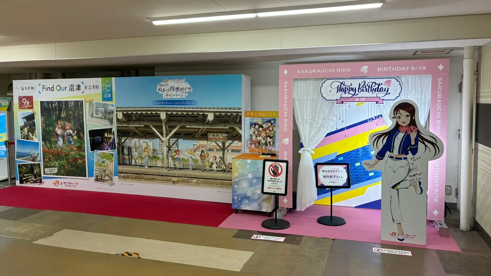 沼津駅南口の特設展示スペース。左に「Find Our 沼津」とAqoursの四季めぐりキャンペーンのパネル、中央にスタンプ台、右にピンクの枠の桜内梨子お誕生日フォトスポット