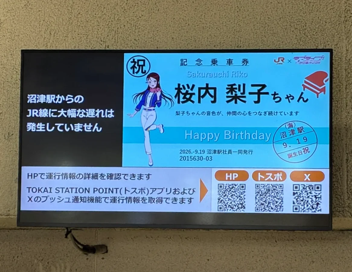 沼津駅南口改札の上の運行情報モニター。左に「沼津駅からのJR線に大幅な遅れは発生していません」、右に記念乗車券風のデザインで「桜内 梨子ちゃん」「Happy Birthday」と、沼津駅の日付印風のスタンプ
