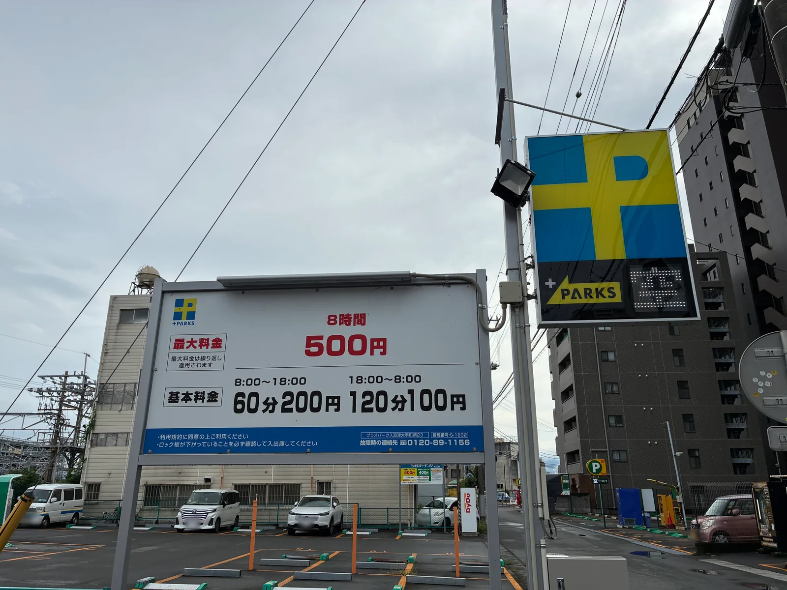 プラスパークス沼津大手町第23の料金看板。最大料金8時間500円（繰り返し適用）、基本料金 8時から18時は60分200円、18時から8時は120分100円。奥にロック板式の駐車スペース
