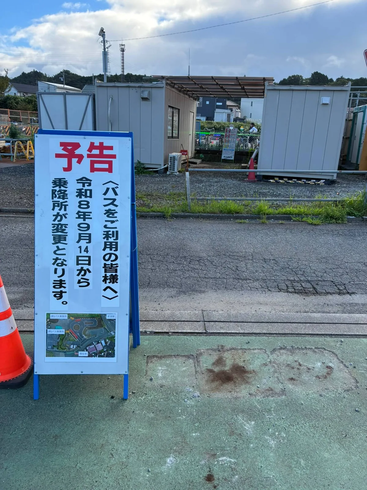 移設後の旧乗降所。予告看板だけが残り、右側の緑色の床にはバス停ポールの台座を撤去した四角い跡が3つ並んでいる
