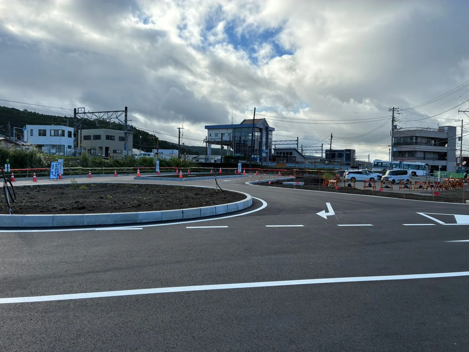 新しいバス乗降所から見た岩波駅の駅舎。間にロータリーの植栽帯と車道があり、右奥に大型バスが停まっている
