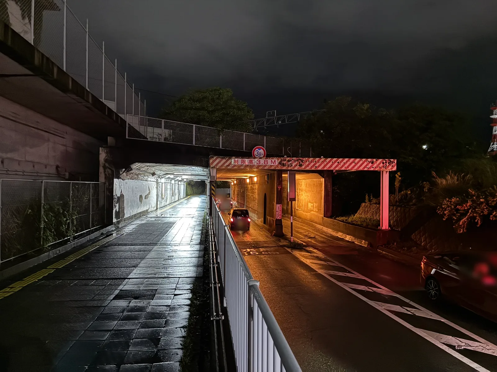 夜の三ツ目ガード北側の入口。赤白の縞模様の門型に「制限高3.8M」の表示があり、その下を車がガードへ入っていく。左側には線路の下をくぐる歩道が別に通っている