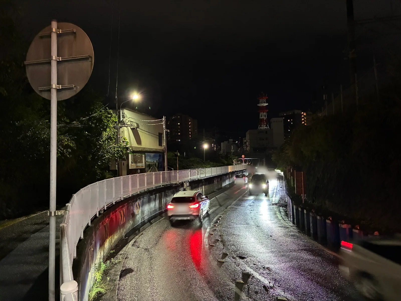 ガードへ向かってカーブしながら下る2車線の坂道。濡れた路面を、下っていく車と上ってくる車がすれ違っている
