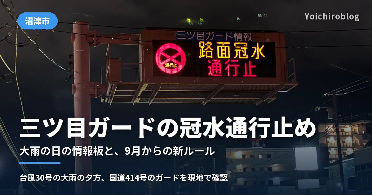 夜の交差点の上に掛かる「三ツ目ガード情報」の電光掲示板。赤い通行止めのマークと「路面冠水 通行止」の文字が光り、奥に濡れた道路とマンションの明かりが見える（2026年10月25日撮影）