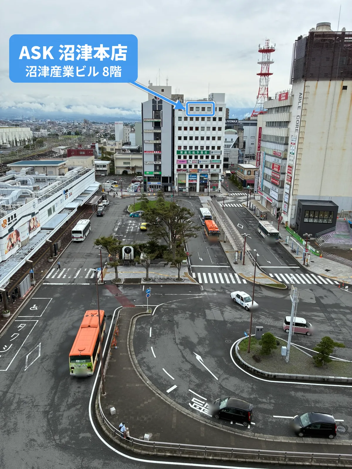 沼津駅南口のバスロータリーの向こうに建つ白い8階建ての沼津産業ビル。最上階の8階の中央を青い枠で囲み、「ASK 沼津本店 沼津産業ビル 8階」のラベルから矢印で示している
