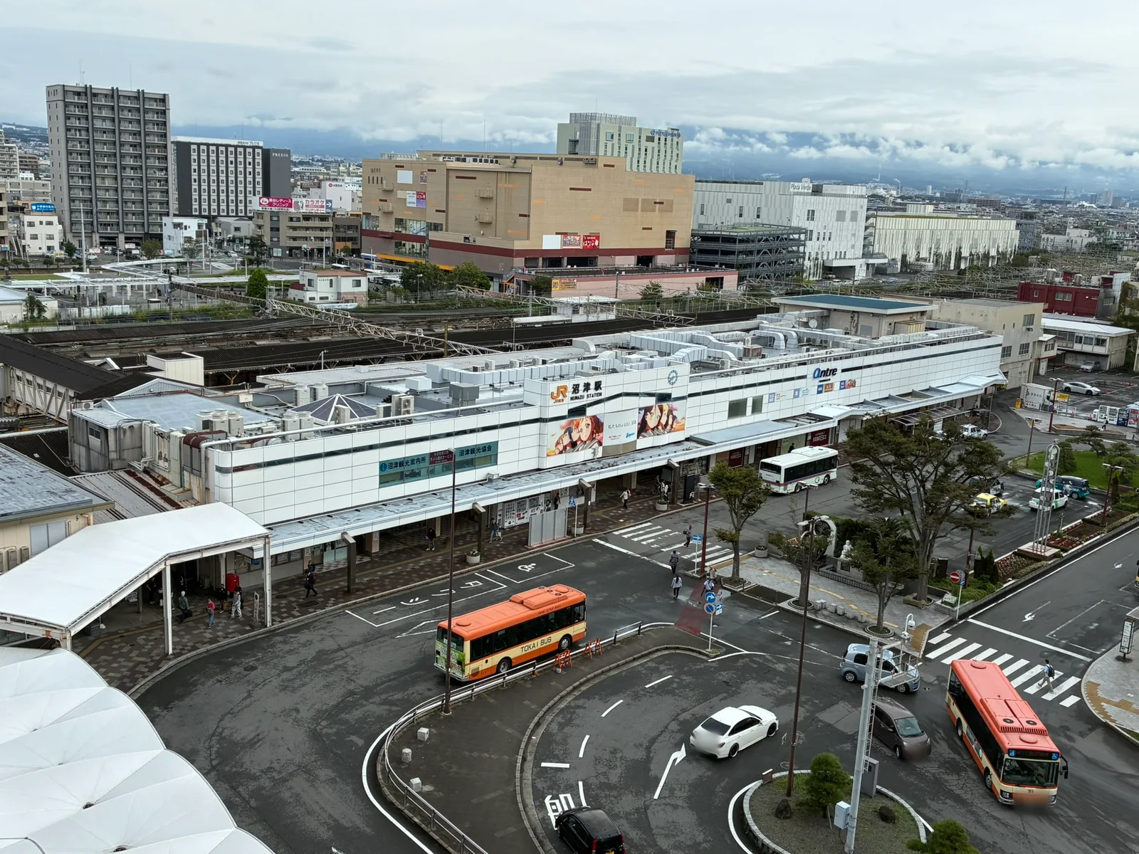 高い位置から見た沼津駅南口。白い駅舎の前にバスロータリーが広がり、路線バスやタクシーが停まっている